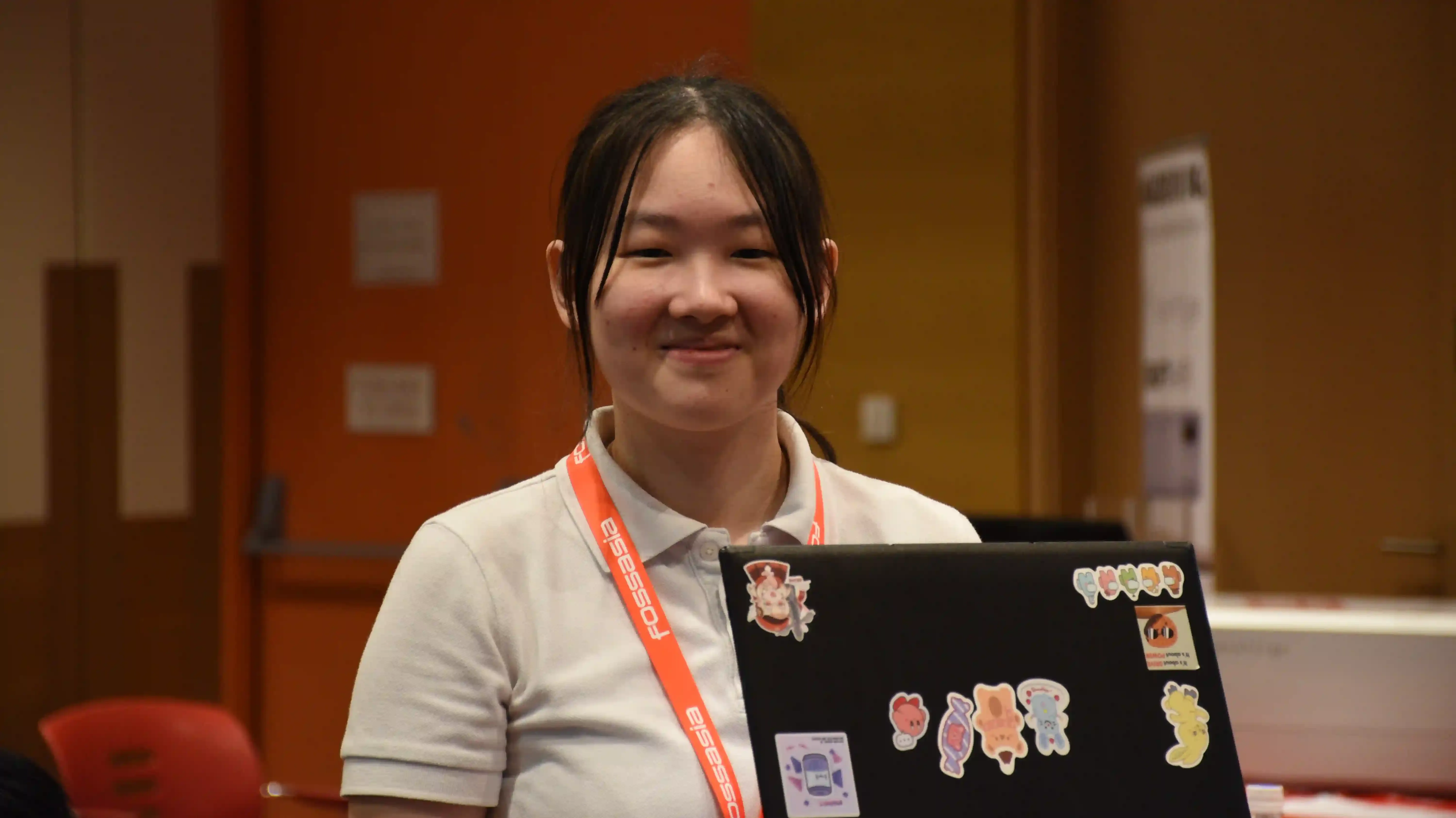 A lady with a FossAsia lanyard holding a laptop in a auditorium